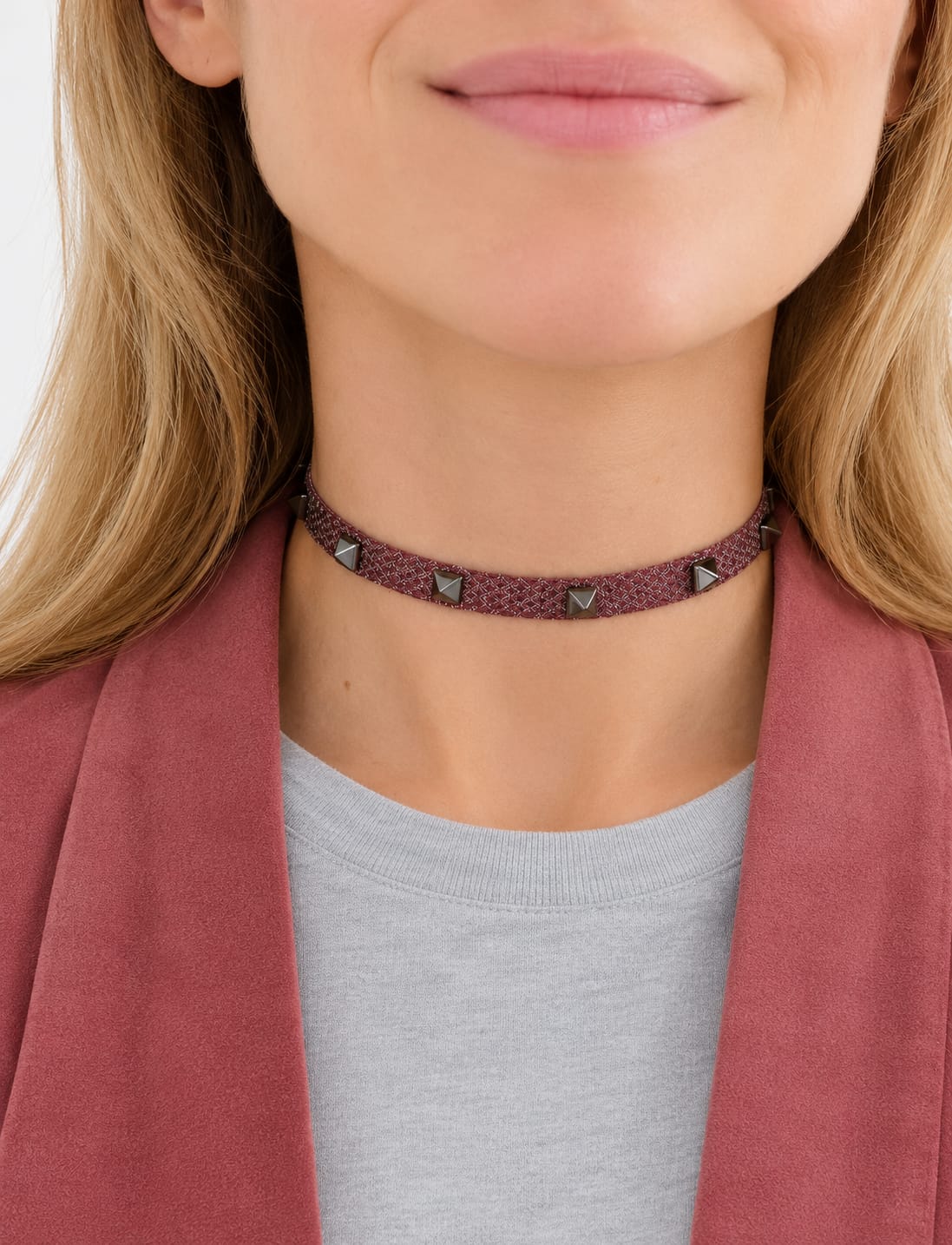Choker Guinda SANUKE con detalles metálicos en plata Choker Guinda de SANUKE con cordón guinda y aplicaciones metálicas plateadas, llevado al cuello con camiseta gris y americana rosa.