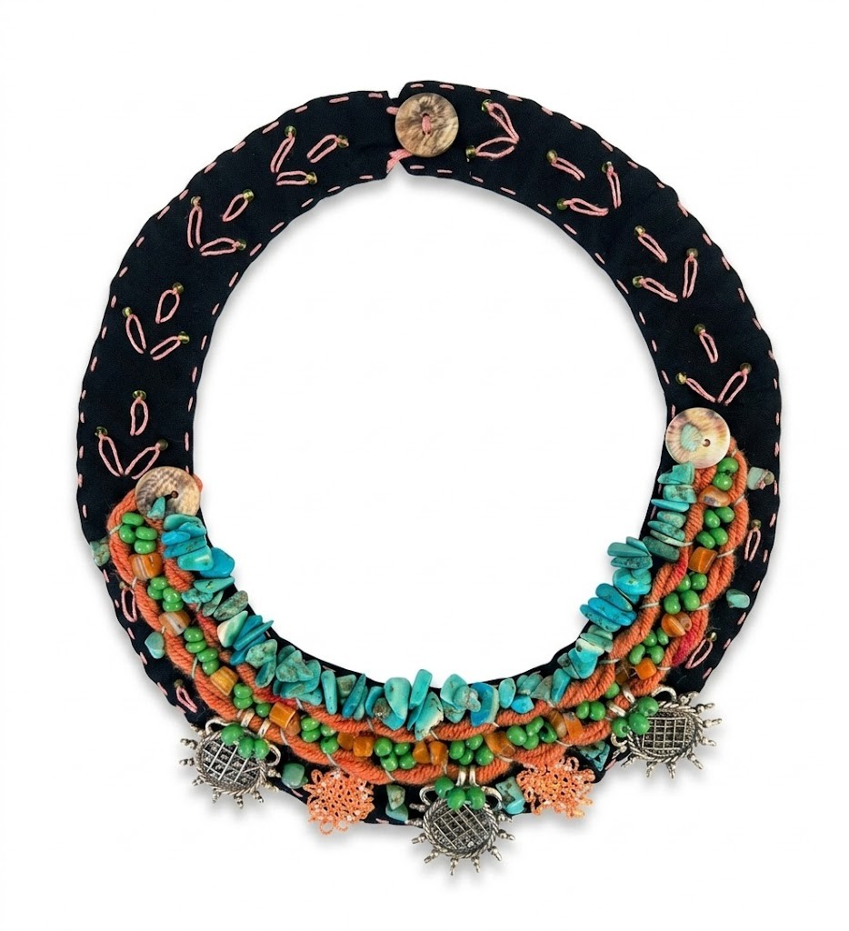 collar-textil-artesanal-timon-coral-turquesa-sanuke. Collar de tela negro bordado a mano de Sanuke con hileras de piedras turquesas, cordón naranja coral, cuentas verdes y dijes plateados con forma de soles
